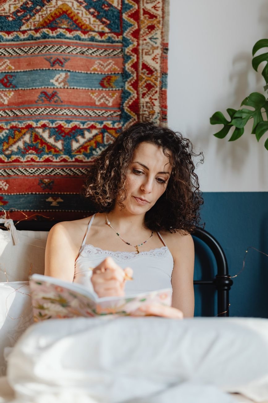 A woman writing in her journal in a cozy bedroom setting, reflecting and resting.